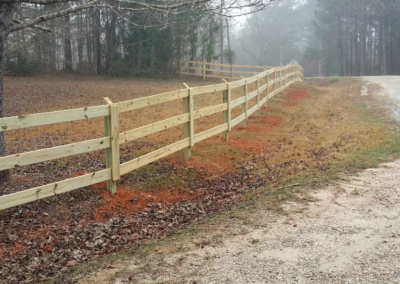 Photo of wood fence along gravel road in pine forest